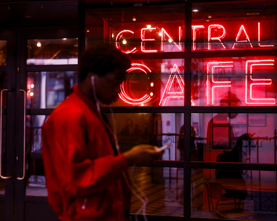 Person in red on the phone walking past the Neon red sign of a cinema in London