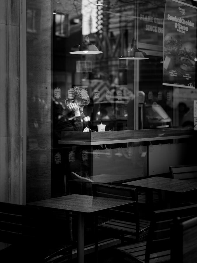 Man sitting at a burger king window eating lunch and using phone