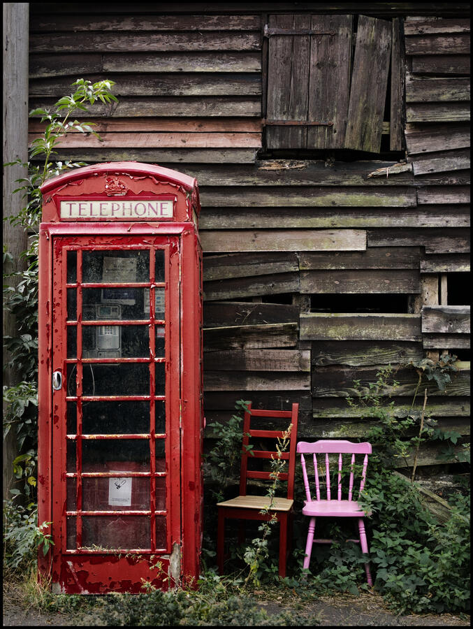 Old overgrown Telephone Kiosk with 2 chairs beside it